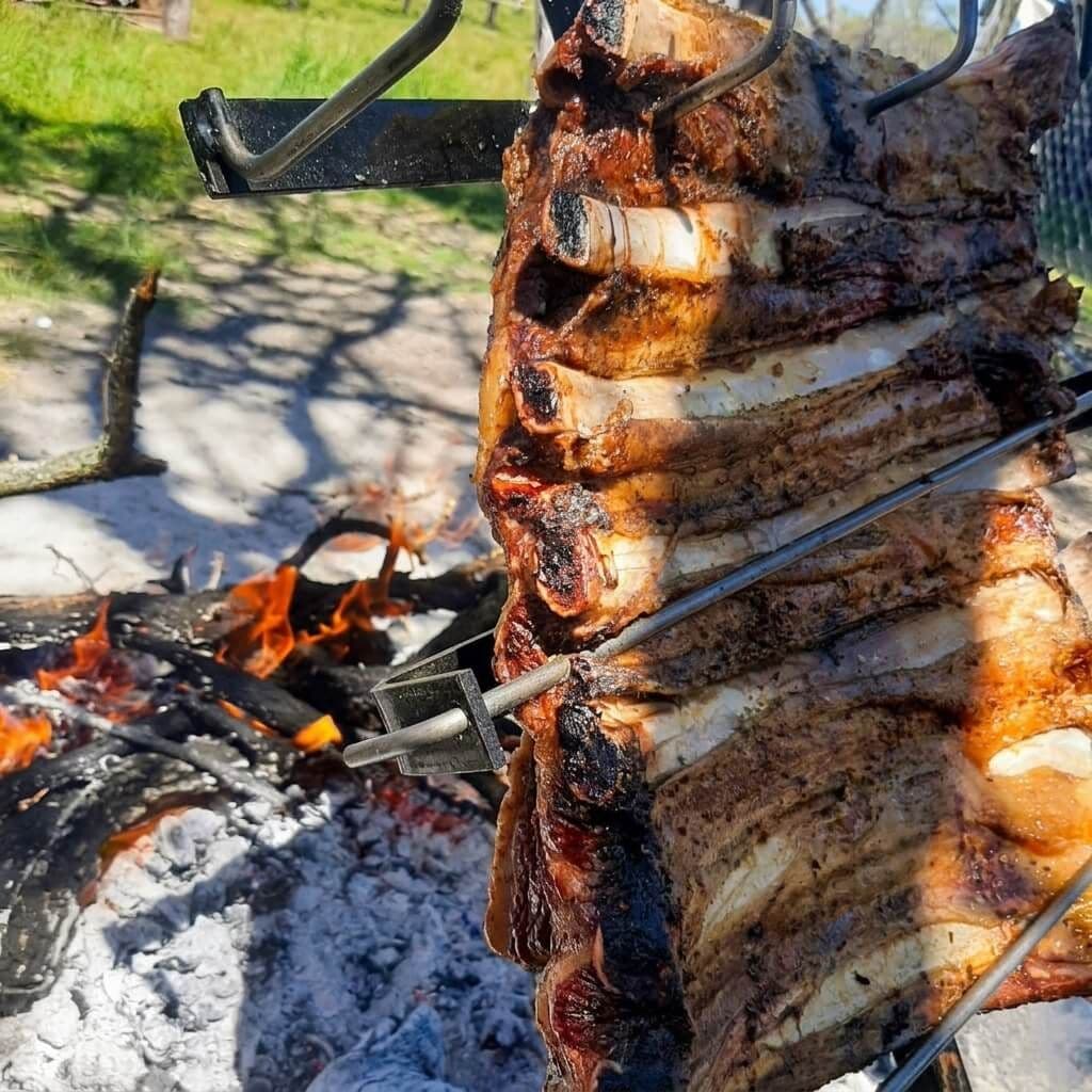 Primer plano del asado de manta dorado en la cruz de hierro, junto al fuego de leña