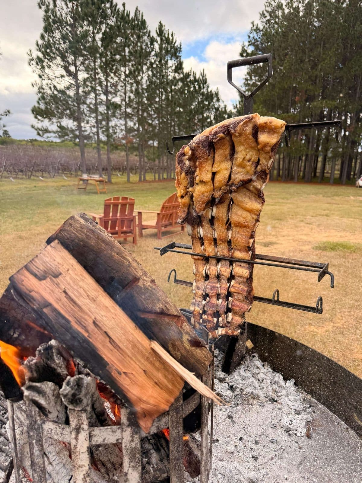 Asado de manta colgado en una cruz de hierro junto al fuego de leña, al aire libre