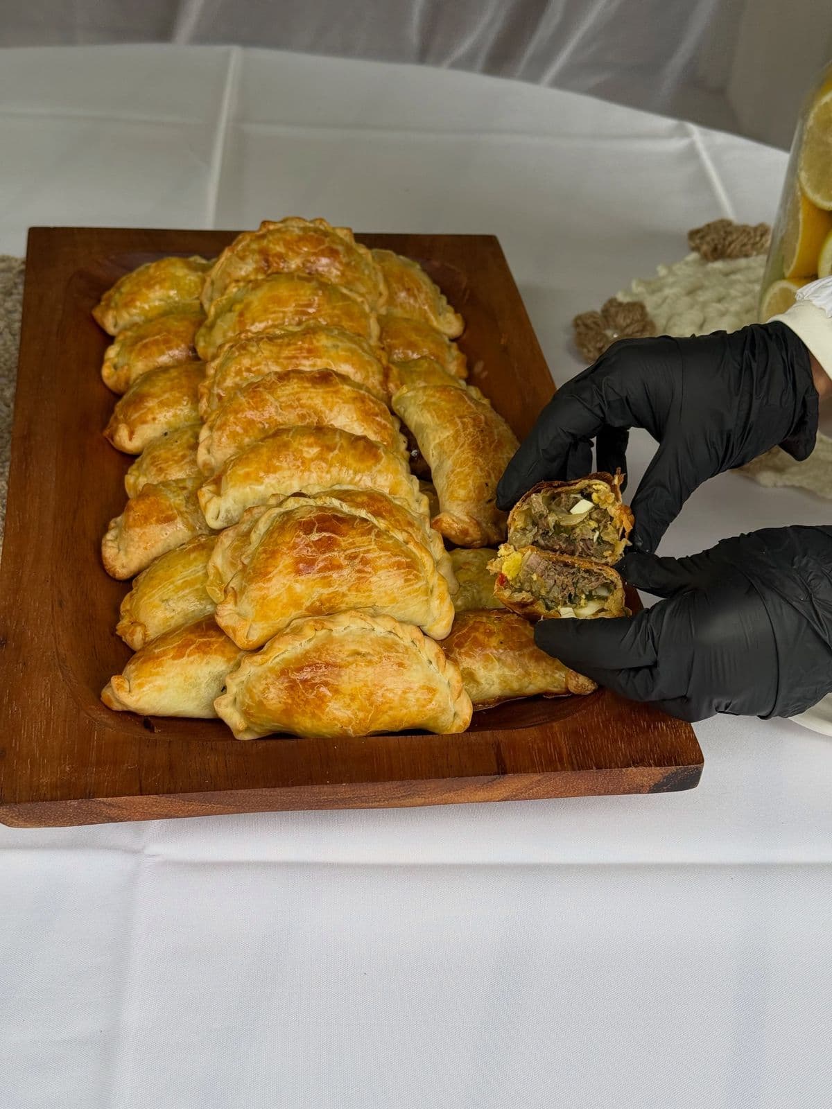 Fuente de madera con empanadas de carne horneadas y una abierta que muestra el relleno
