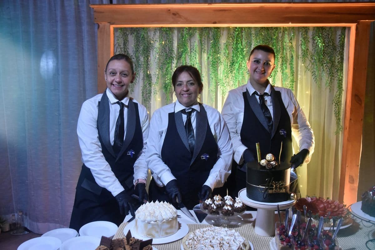 Tres mozas con chaleco de Jorge Luis y guantes sirviendo tortas en la mesa dulce de un cumpleaños